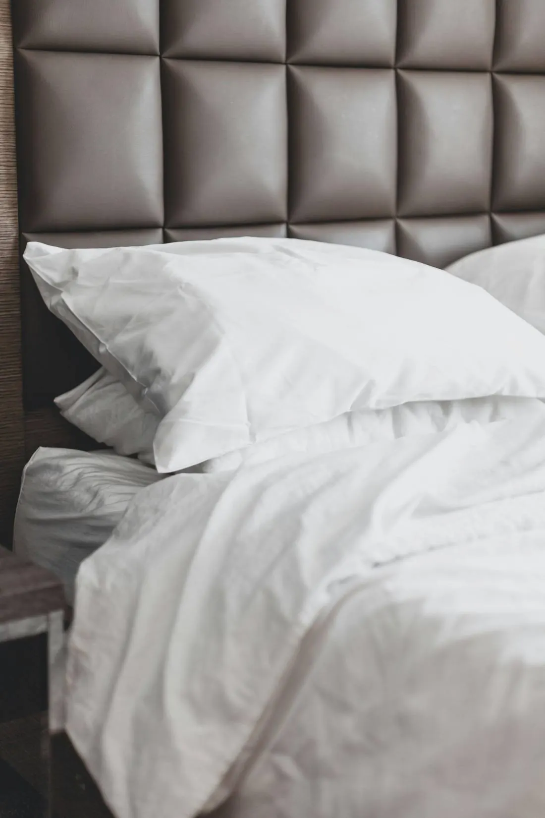 Almohadas y nórdico blancos sobre una cama con cabecero tapizado